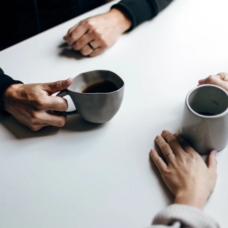 Two people having coffee. Arms and cups are visible on the table